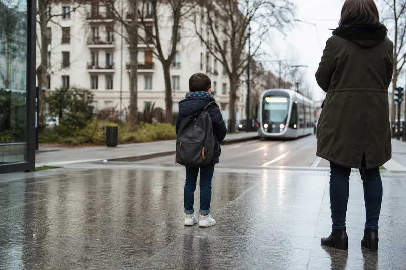 Un enfant et une femme attendent un tramway sur un trottoir mouillé par la pluie