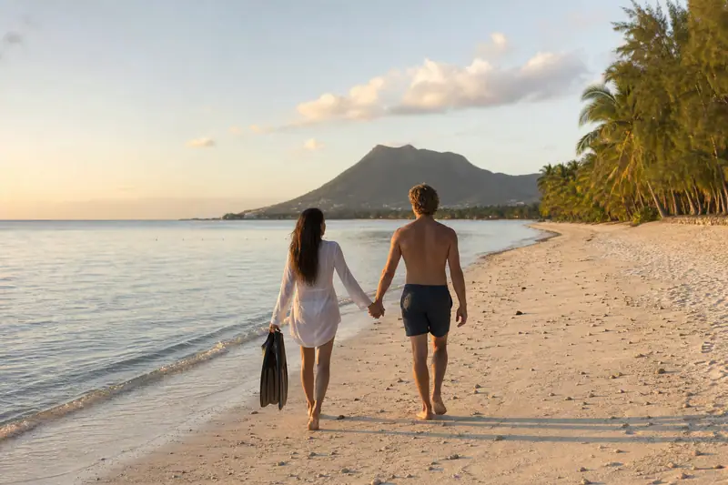 Un couple marche main dans la main sur une plage, face à une montagne sombre