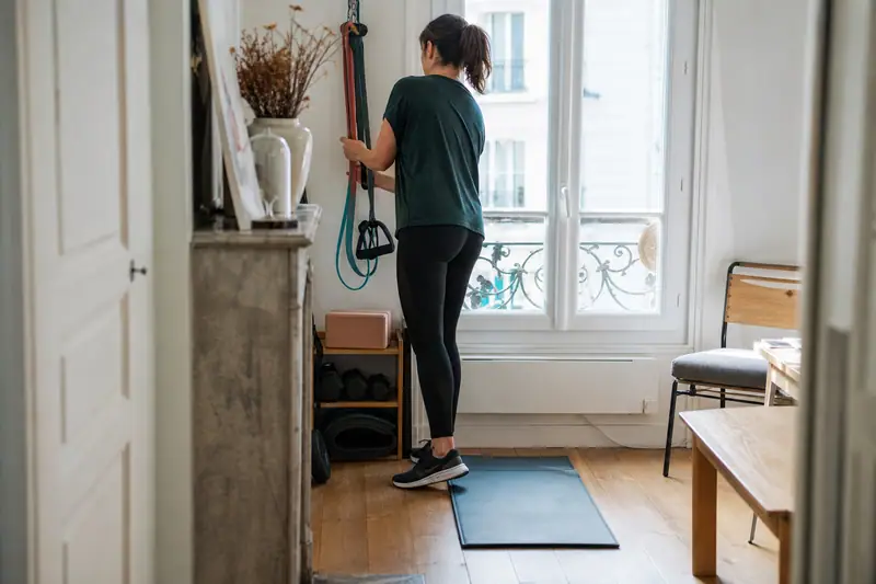 Une femme range des élastiques près d'un tapis bleu dans un appartement lumineux