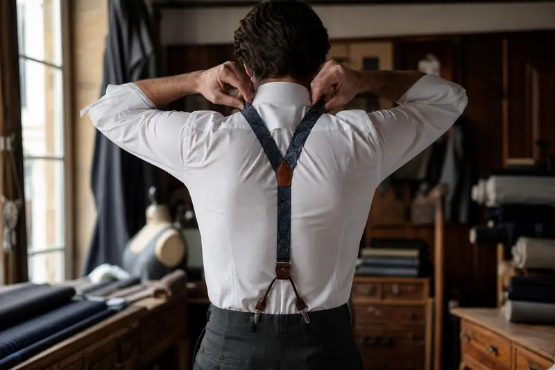 Un homme ajuste des bretelles sombres sur sa chemise blanche dans un atelier de tailleur