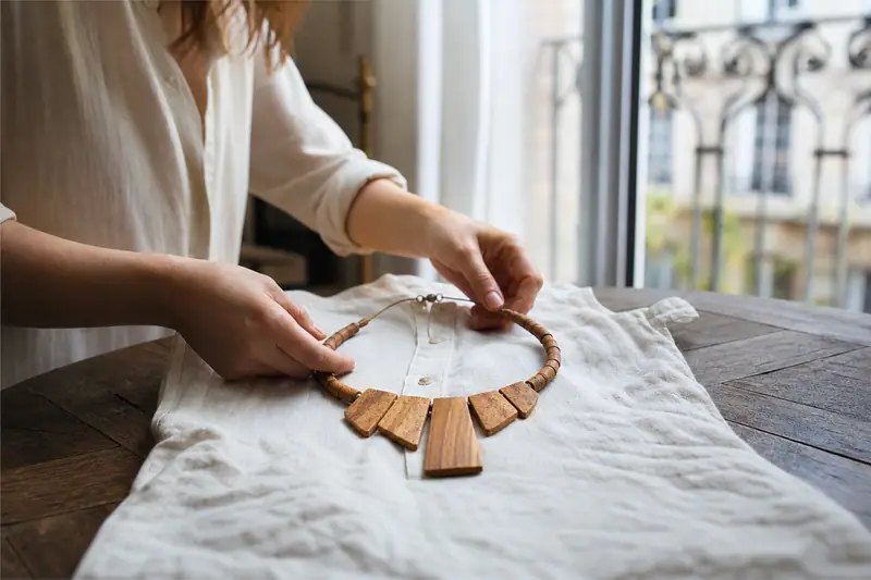 Une personne dispose un collier de perles et pendentifs en bois sur un tissu blanc