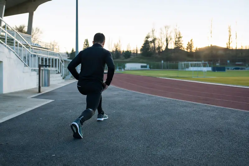 Un homme en tenue noire effectue une fente sur une piste d'athlétisme au coucher du soleil