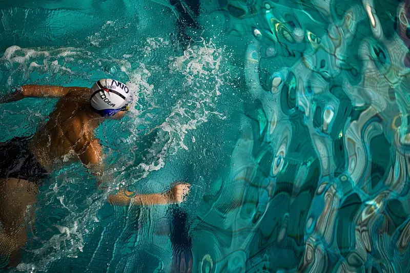 Nageur en bonnet blanc et lunettes avançant dans une piscine turquoise, bras écartés sous l’eau