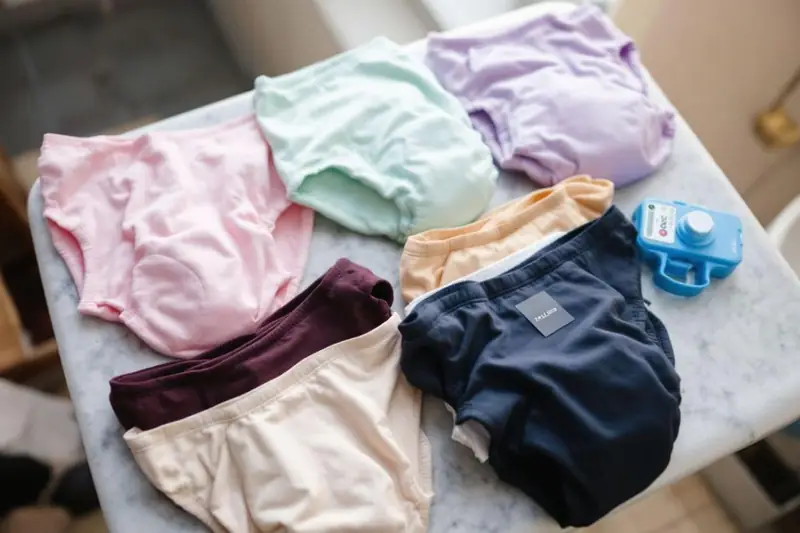 Six culottes colorées sont disposées sur une table grise près d’un petit objet bleu