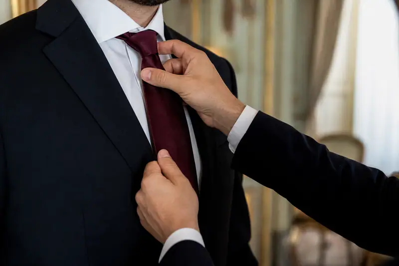 Deux mains ajustent une cravate bordeaux sur une chemise blanche et un costume noir