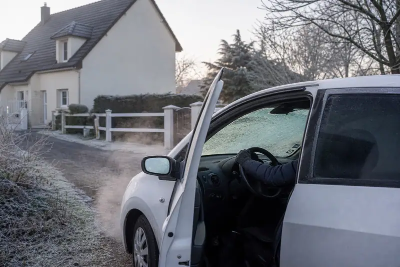 Voiture blanche garée devant une maison, portière ouverte et pare-brise couvert de givre