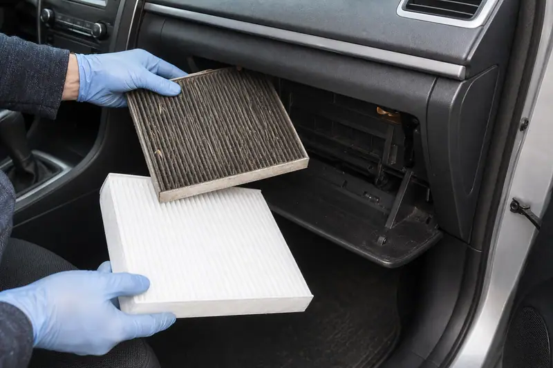 Des mains gantées tiennent deux filtres devant la boîte à gants ouverte d'une voiture