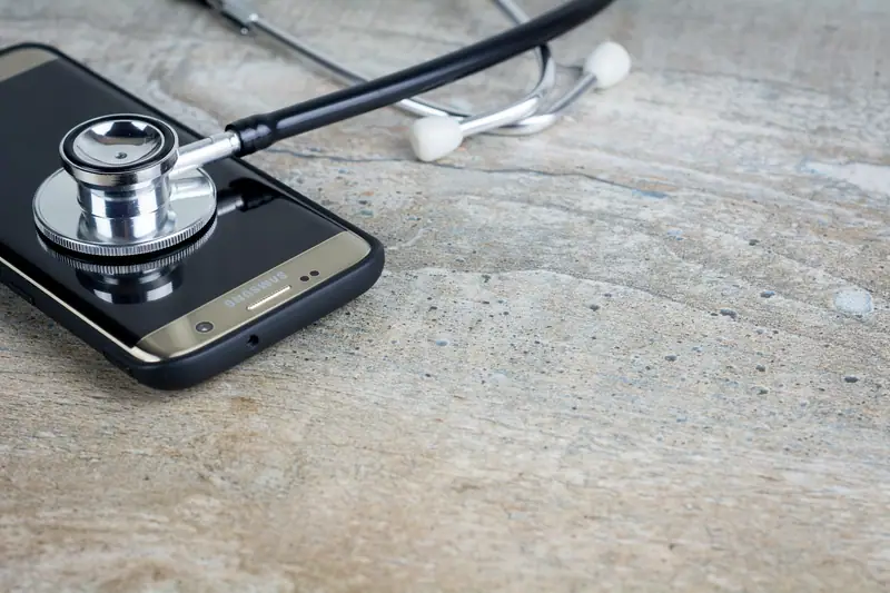 Un smartphone noir posé sur une table en bois avec un stéthoscope métallique