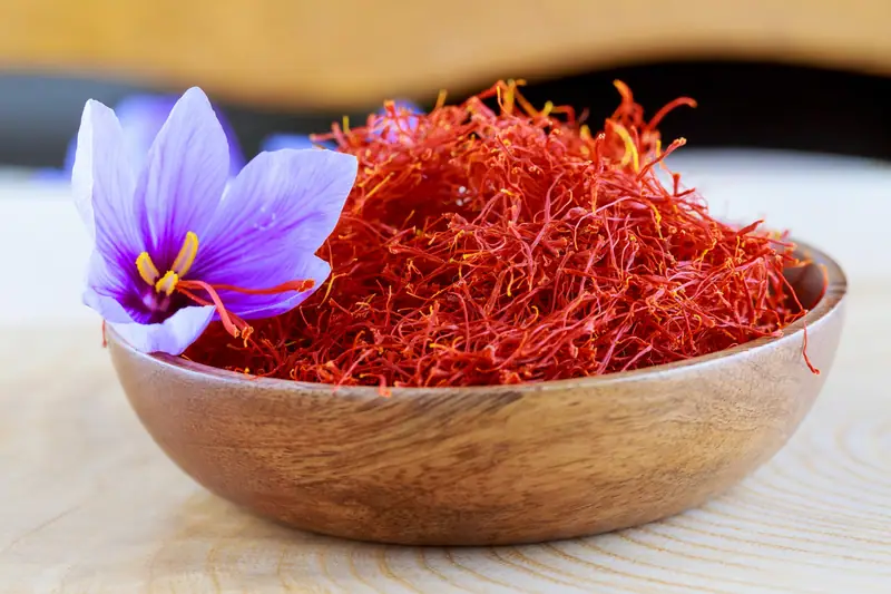 Une fleur violette repose contre un bol en bois rempli de filaments rouges