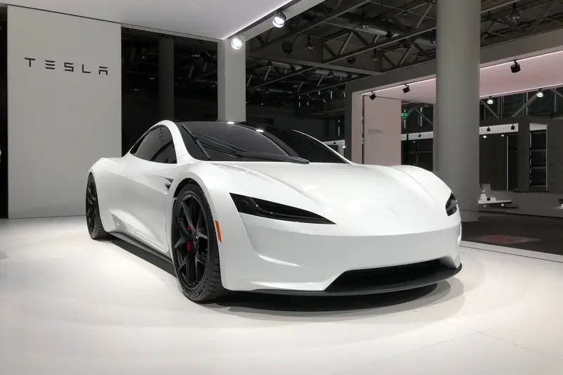 Voiture blanche Tesla exposée sur un sol clair dans un showroom aux murs gris