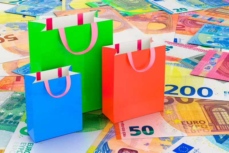 Trois sacs cadeaux colorés posés sur un tapis de billets en euros multicolores