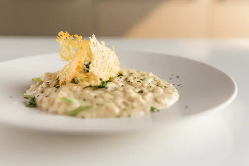 Assiette blanche de riz crémeux parsemé d’herbes, surmonté de fines tuiles dorées