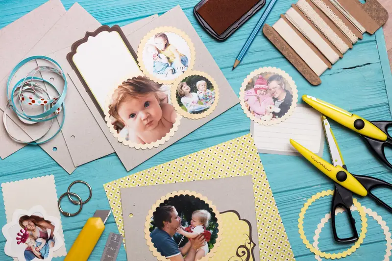 Photos découpées, papiers colorés, ciseaux et rubans disposés sur une table en bois turquoise