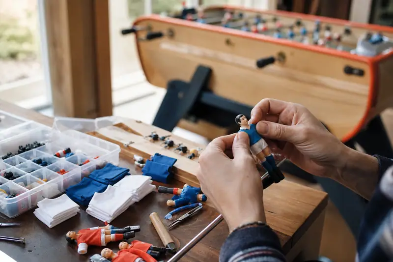 Des mains manipulent une figurine bleue sur une table couverte de petites pièces de baby-foot