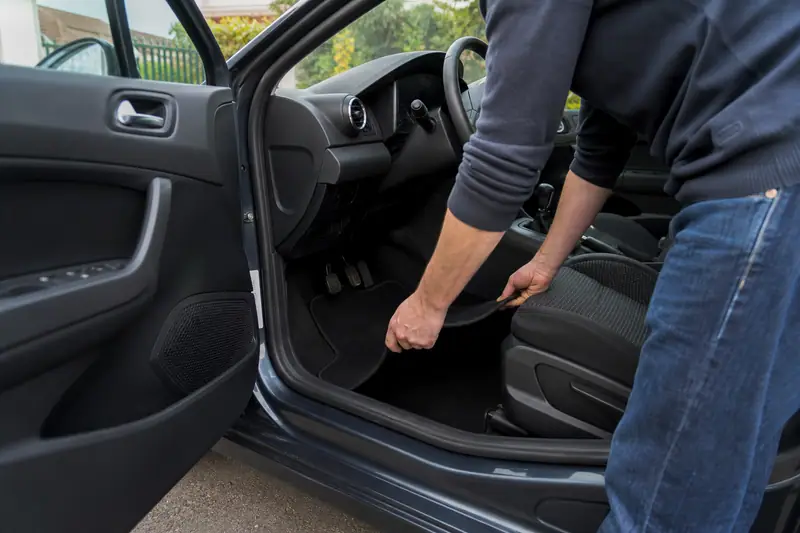 Une personne installe un tapis noir dans l’espace pieds d’une voiture ouverte