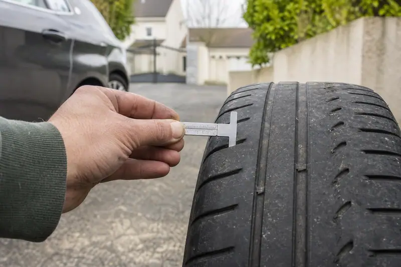 Une main mesure la profondeur des rainures d'un pneu avec une jauge métallique