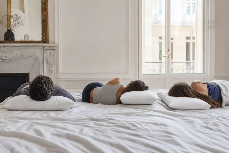 Trois personnes allongées dans des positions différentes sur un lit à draps blancs