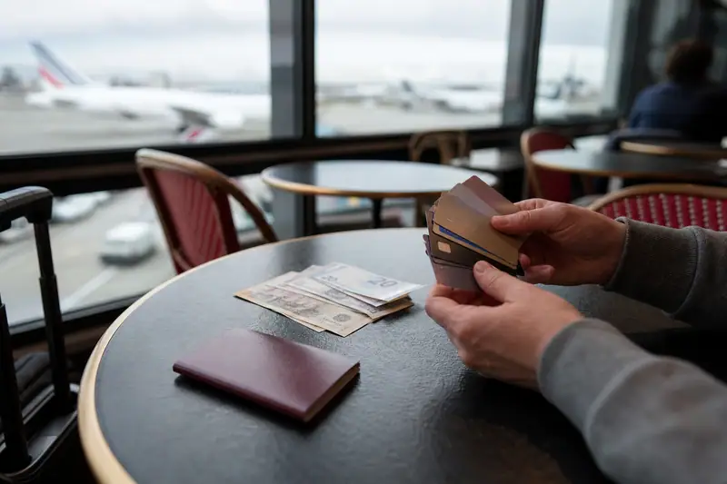 Des mains tiennent plusieurs cartes bancaires au-dessus d'une table avec passeport et billets