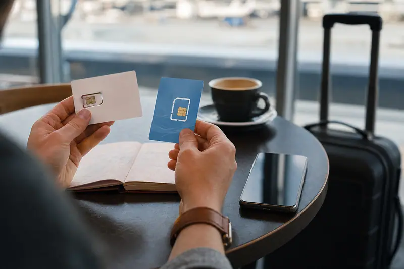 Une personne tient deux cartes SIM au-dessus d'une table avec téléphone, café et valise noire