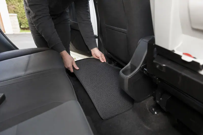Une personne installe un tapis noir texturé au sol derrière le siège avant d’une voiture